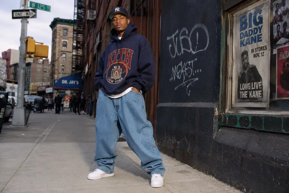 A person wearing classic 90s hip hop fashion including baggy jeans, a snapback cap, and chunky sneakers on a city street