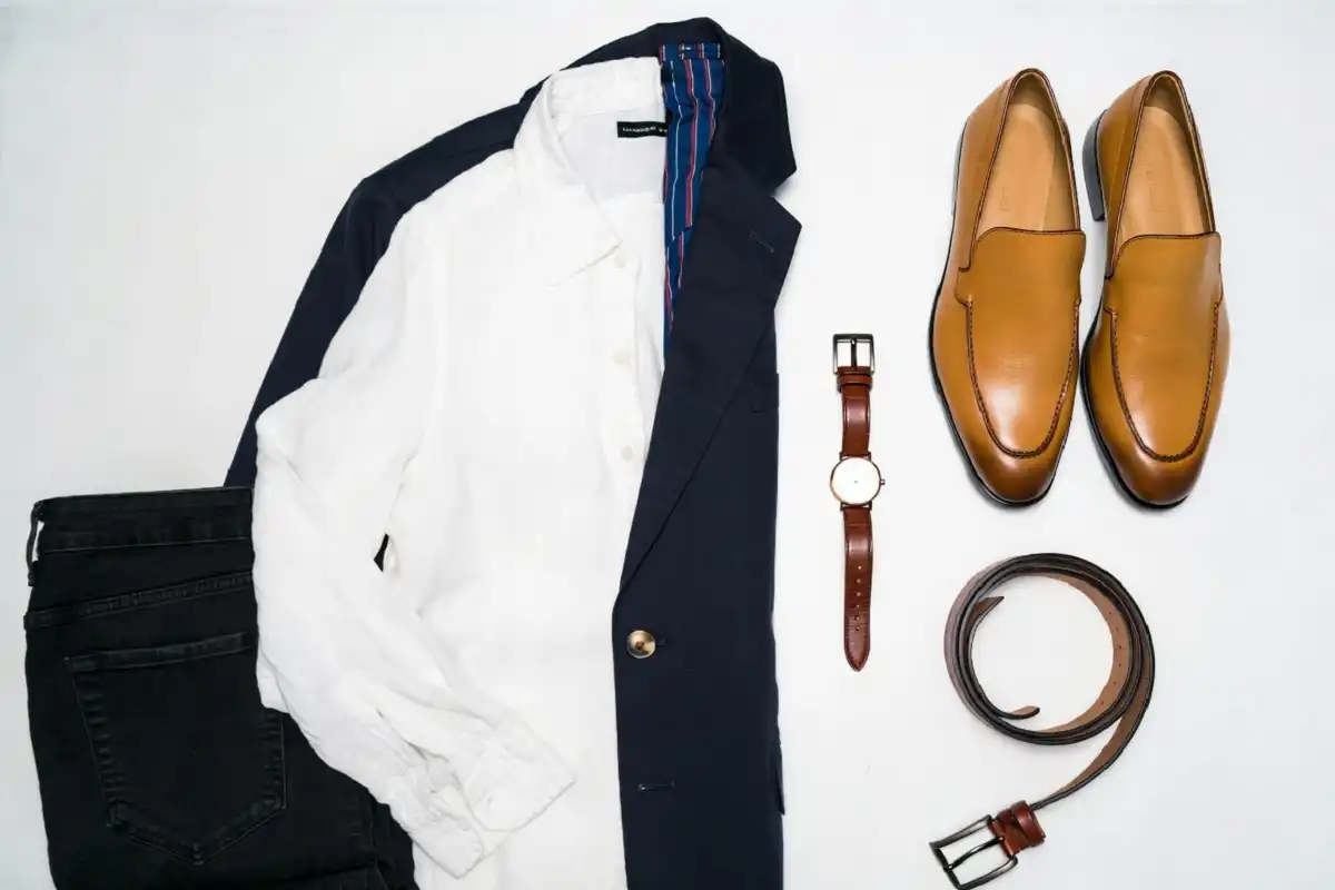 Capsule wardrobe flat lay with white shirt, navy blazer, dark jeans, tan loafers, and accessories
