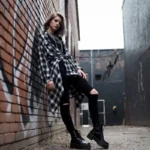 Young woman in grunge fashion outfit wearing flannel shirt, ripped jeans, and combat boots in an urban setting