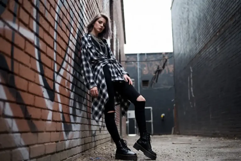 Young woman in grunge fashion outfit wearing flannel shirt, ripped jeans, and combat boots in an urban setting
