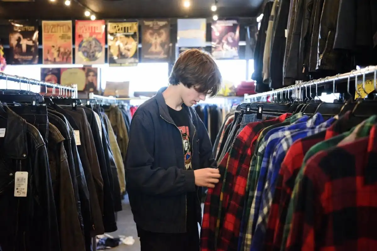 Person browsing flannel shirts and vintage clothing at a thrift store to build a grunge fashion wardrobe