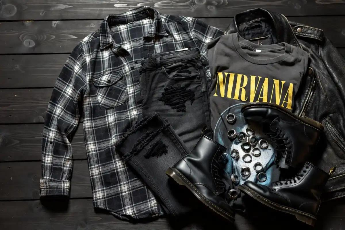 Grunge fashion wardrobe flatlay featuring flannel shirts, ripped jeans, combat boots, and band tees on a dark surface