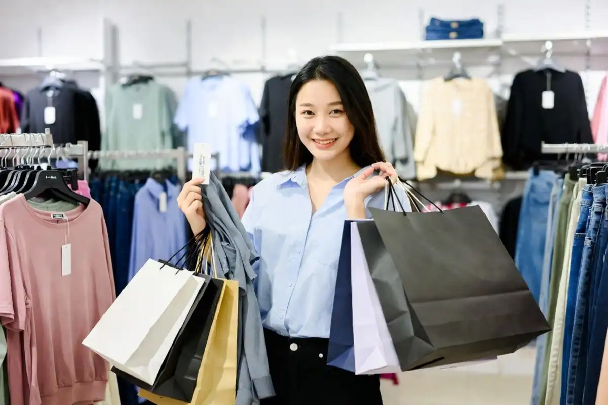 Shopper checking a price tag while holding clothes and shopping bags