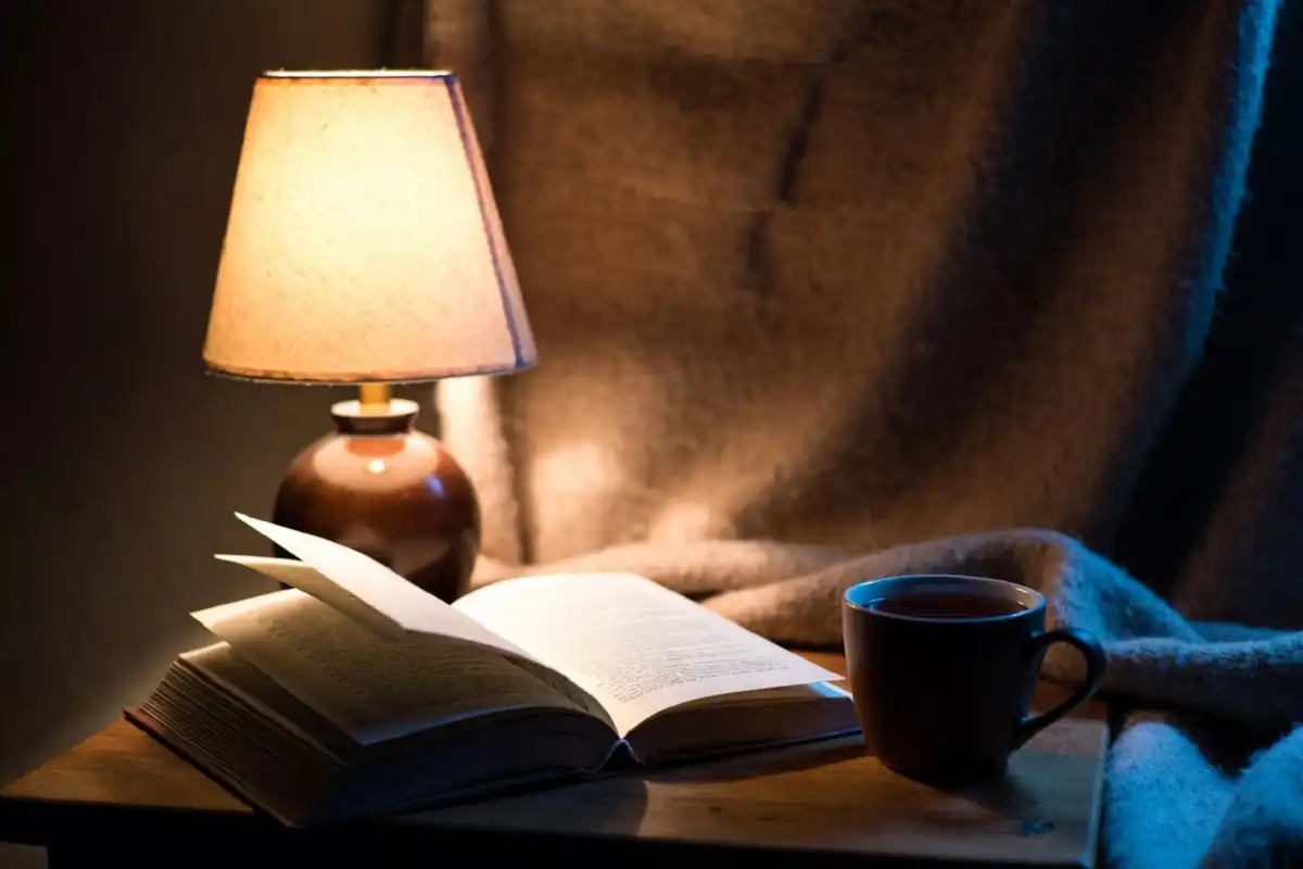 Cozy evening setup with warm lamp, book, and tea for relaxation