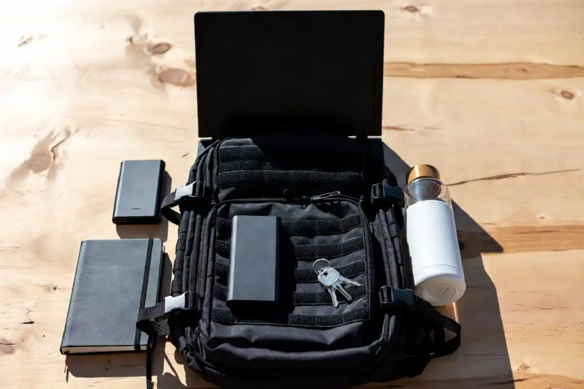 Tactical backpack with laptop, water bottle, and gear laid out for everyday carry